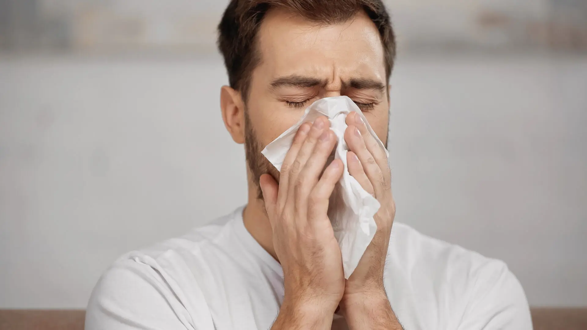 man with allergy sneezing in napkin at home